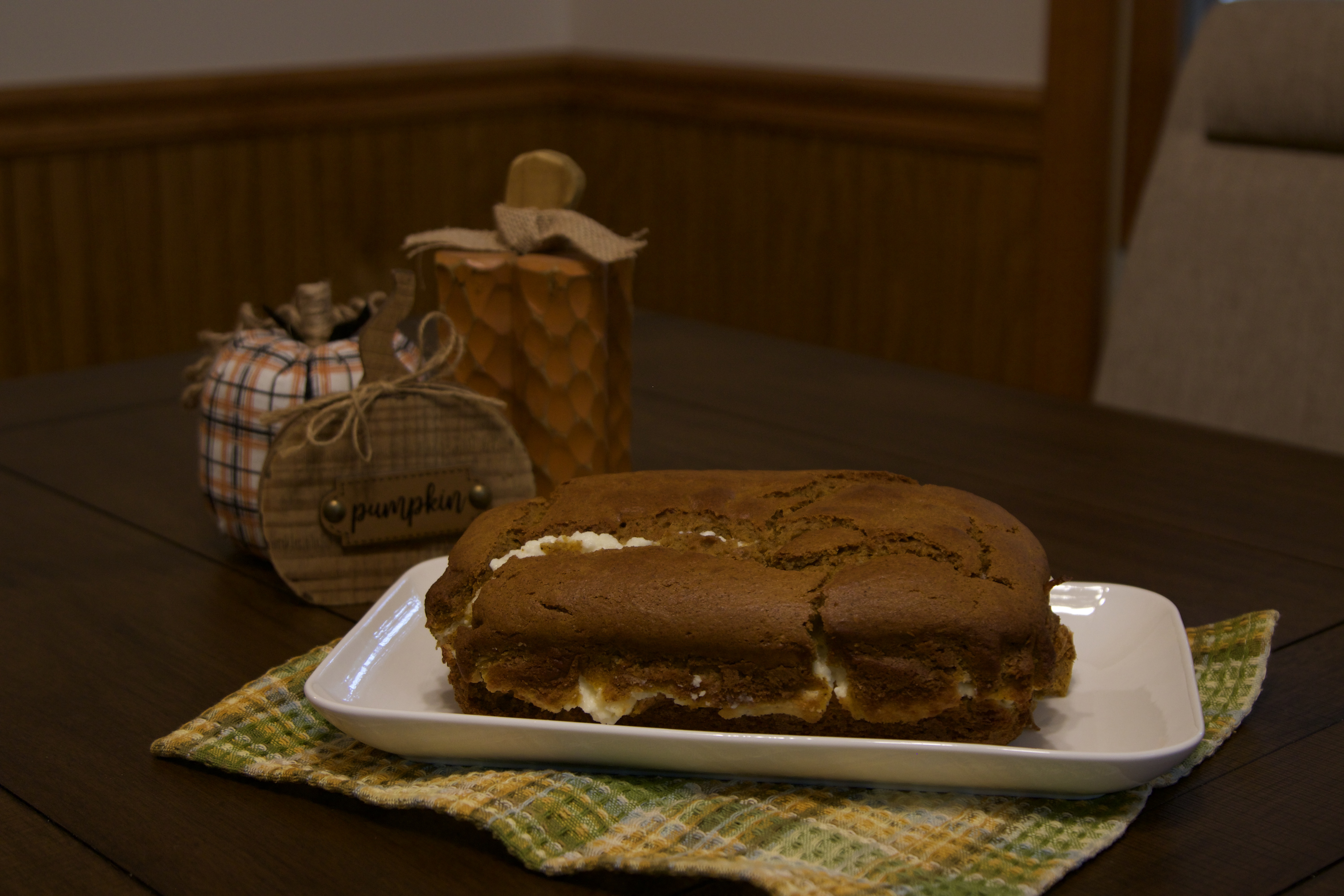 A pumpkin loaf sitting on a platter on the table with decorative pumpkins sitting on the table