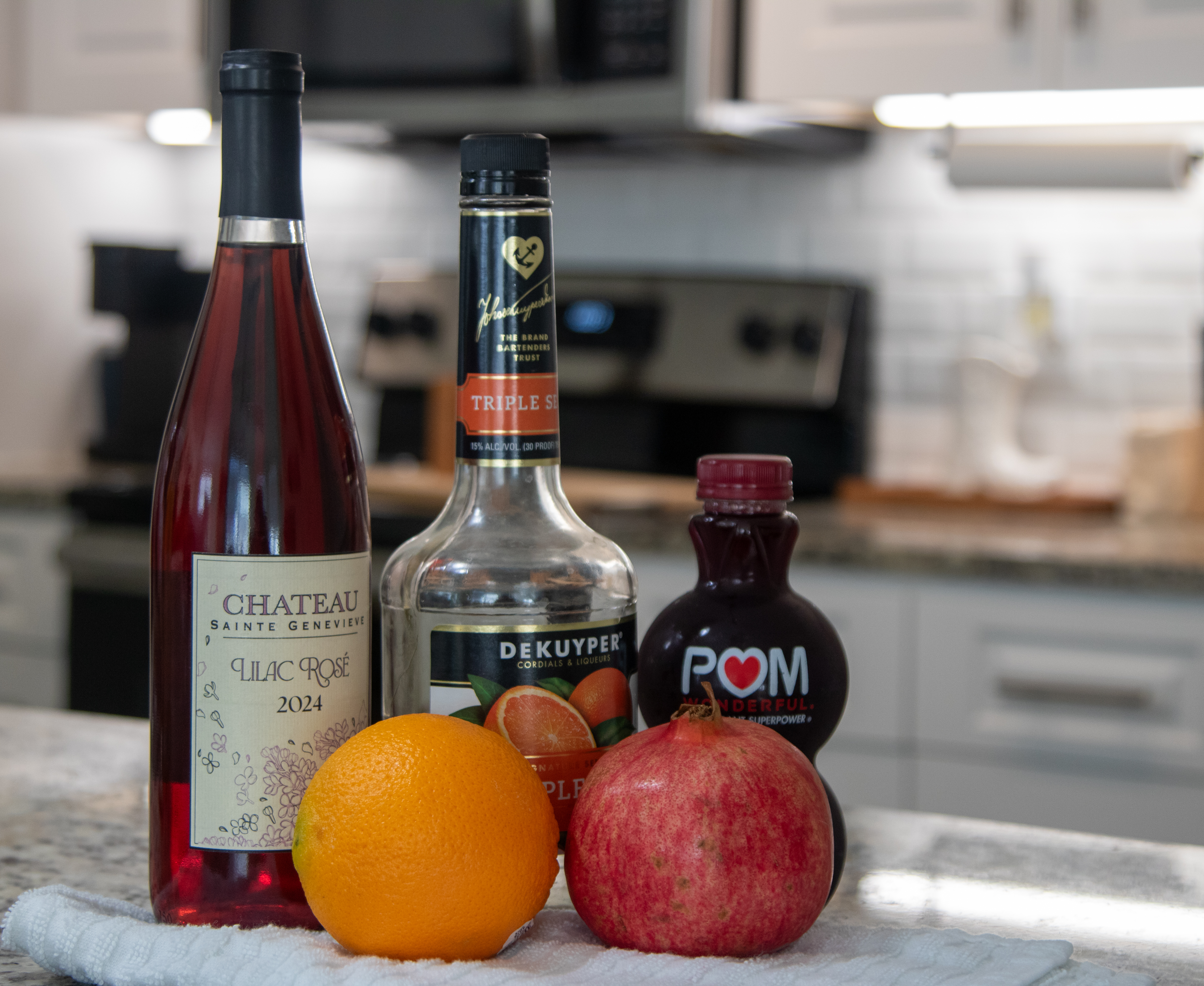 Ingredients shot in a kitchen. Rose wine, triple sec, pomegranate juice, with an orange and pomegranate fruit in front.