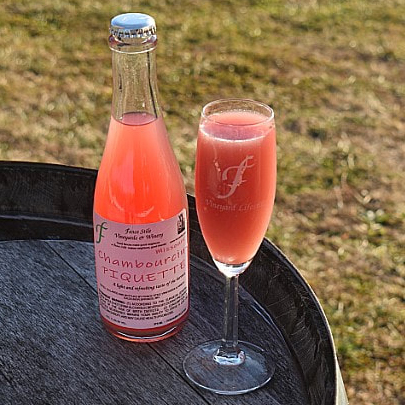 Bottle and flute of Chambourcin Piquette on a barrel outside