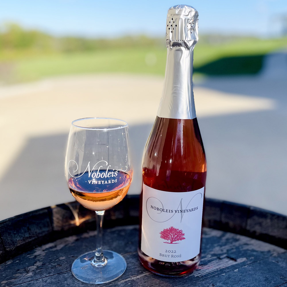 Bottle and glass of Noboleis Brut Rose on a barrel outside