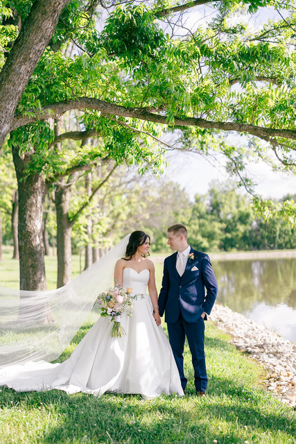 Bride and groom standing in grass with a pond to the side of them