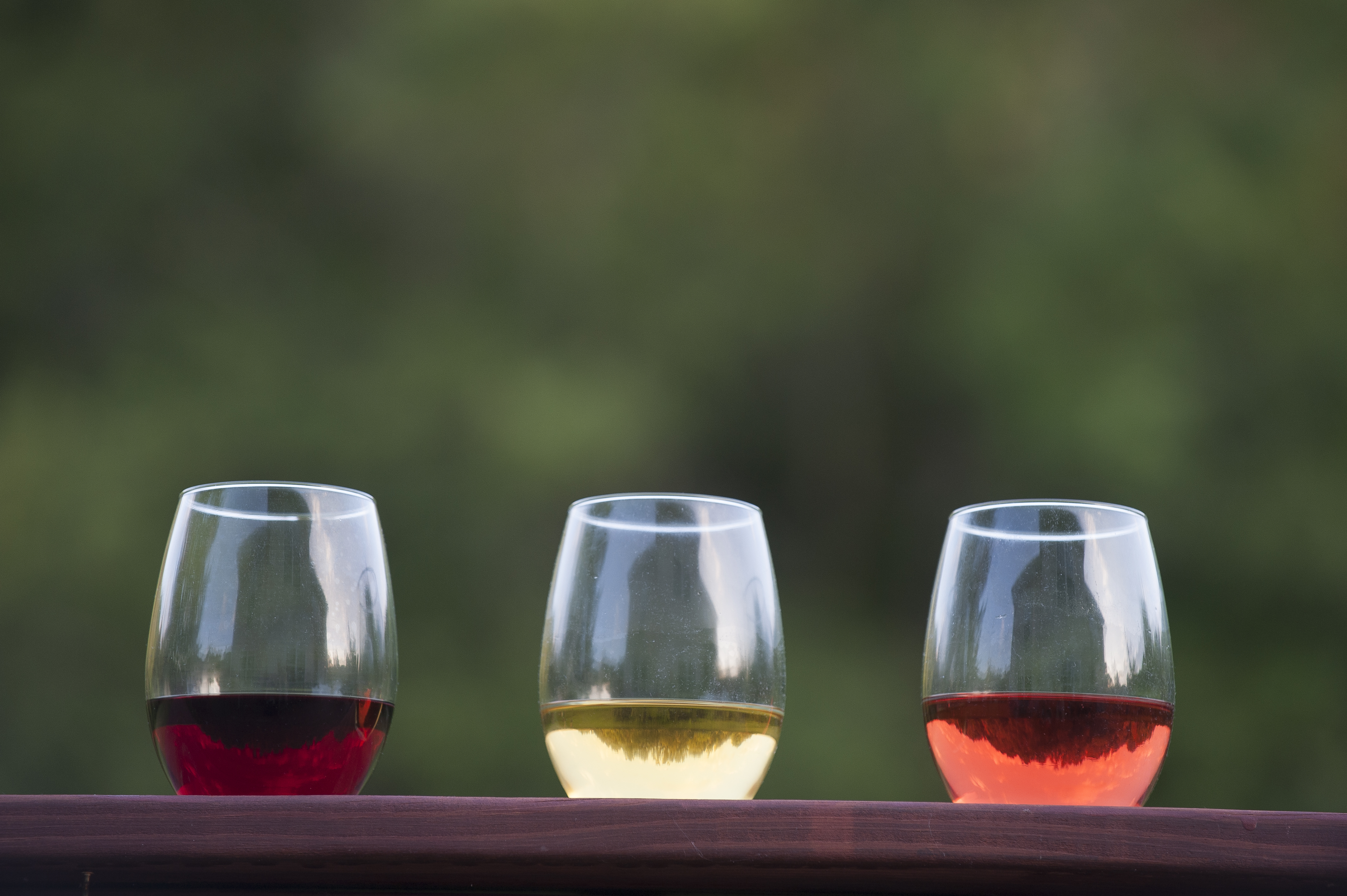 Three glasses of red, white, rosé wine sitting on a ledge.