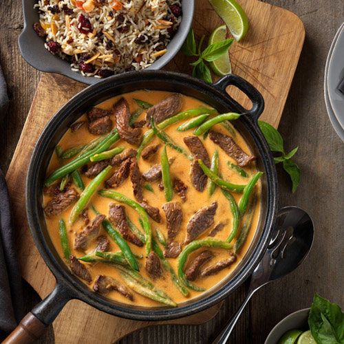 beef curry with rice, fresh basil and lime wedges as garnish