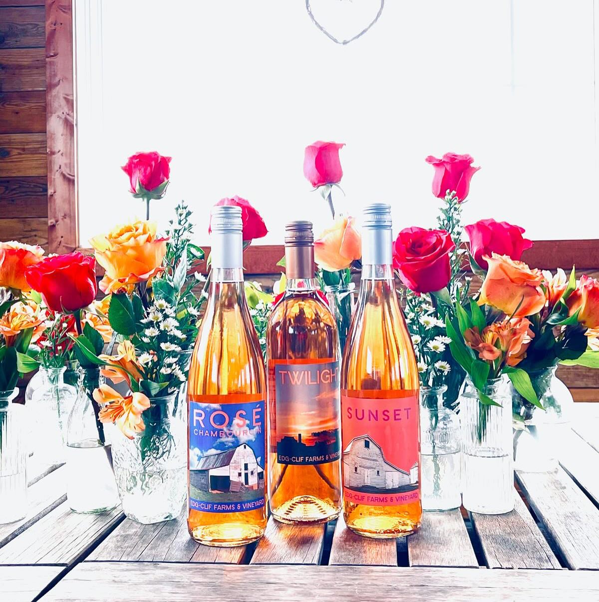 flowers in vases with wine bottles in front of them sitting on a wooden table